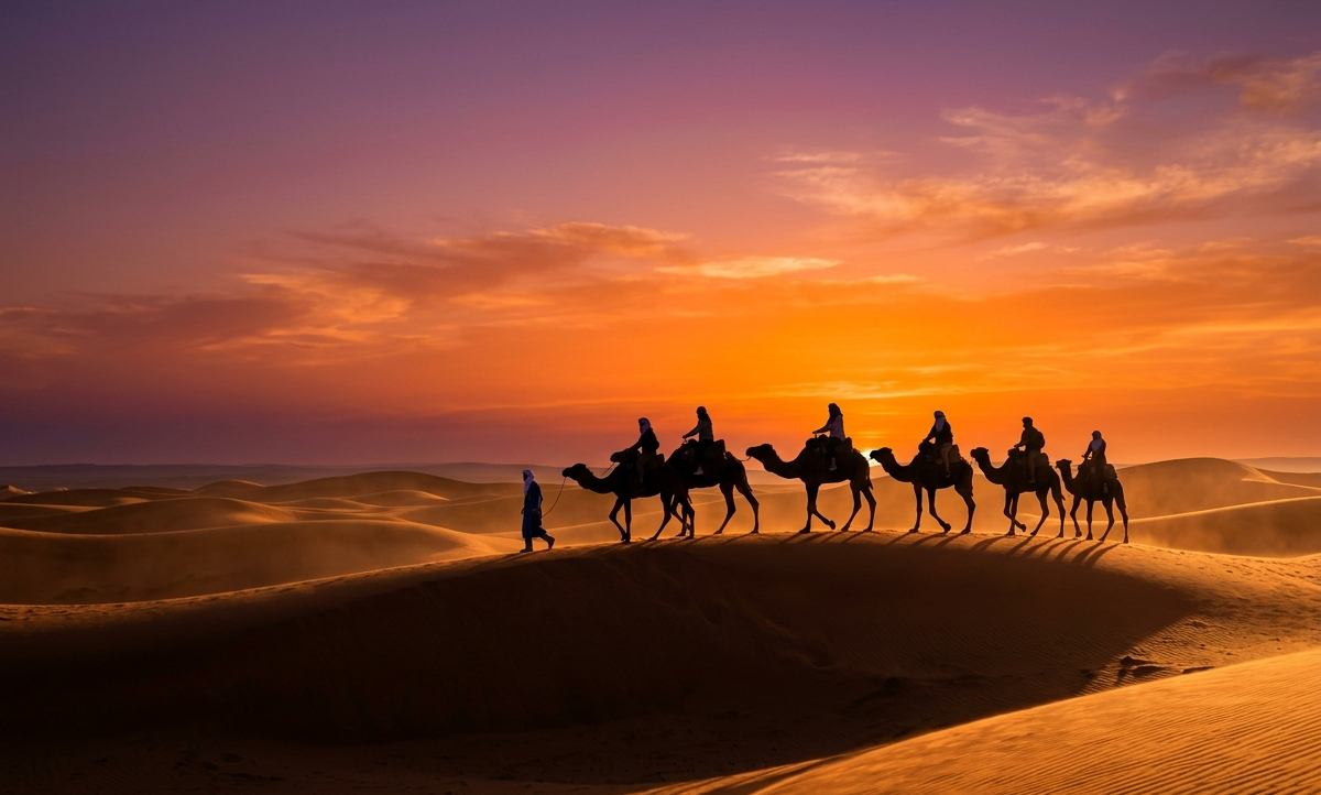 Travelers riding camels across Sahara Desert dunes at sunset in Morocco