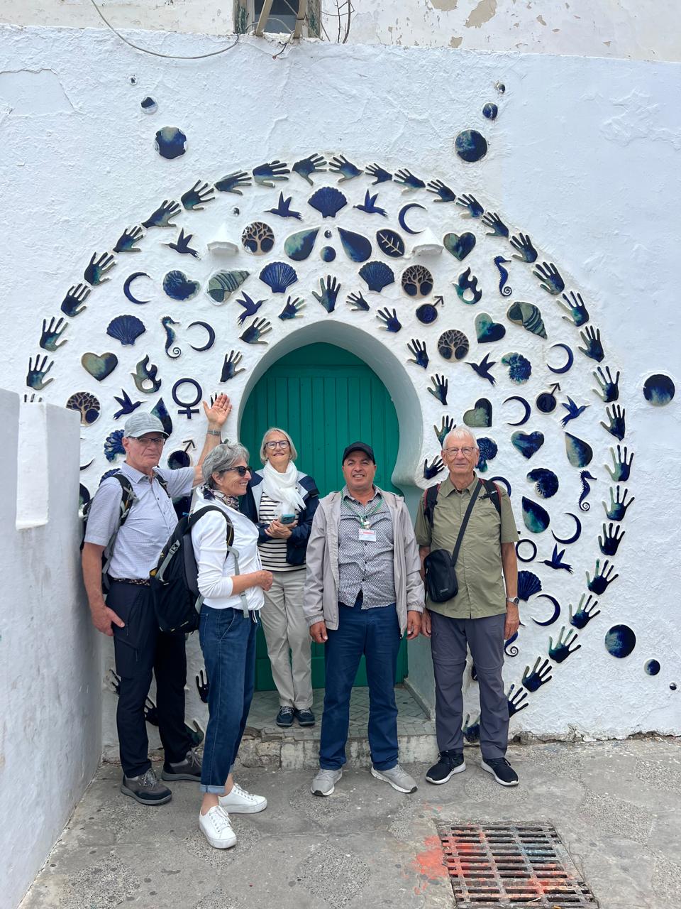 Guide and four guests in front of a blue-tile arch in Asilah