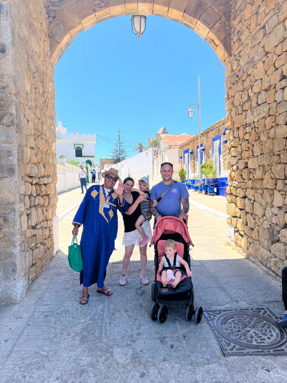 Guide and a family with a stroller under a stone arch in Asilah