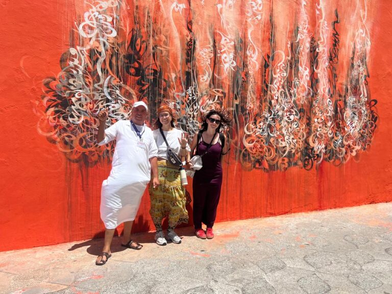 Local guide and two guests in front of a red calligraphy mural in Tangier